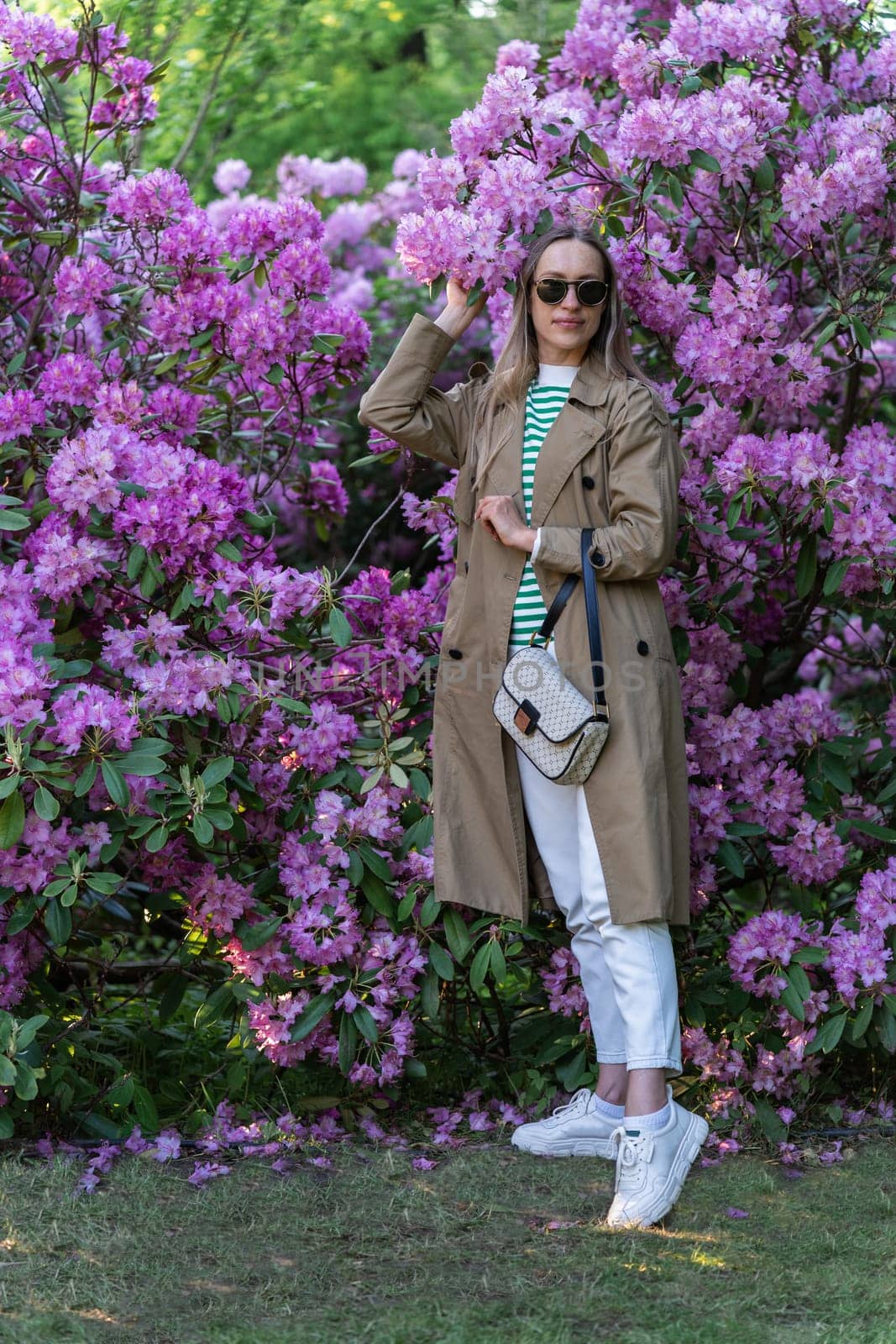 Long-haired woman in sunglasses vohle of a lushly blooming rhododendron bush