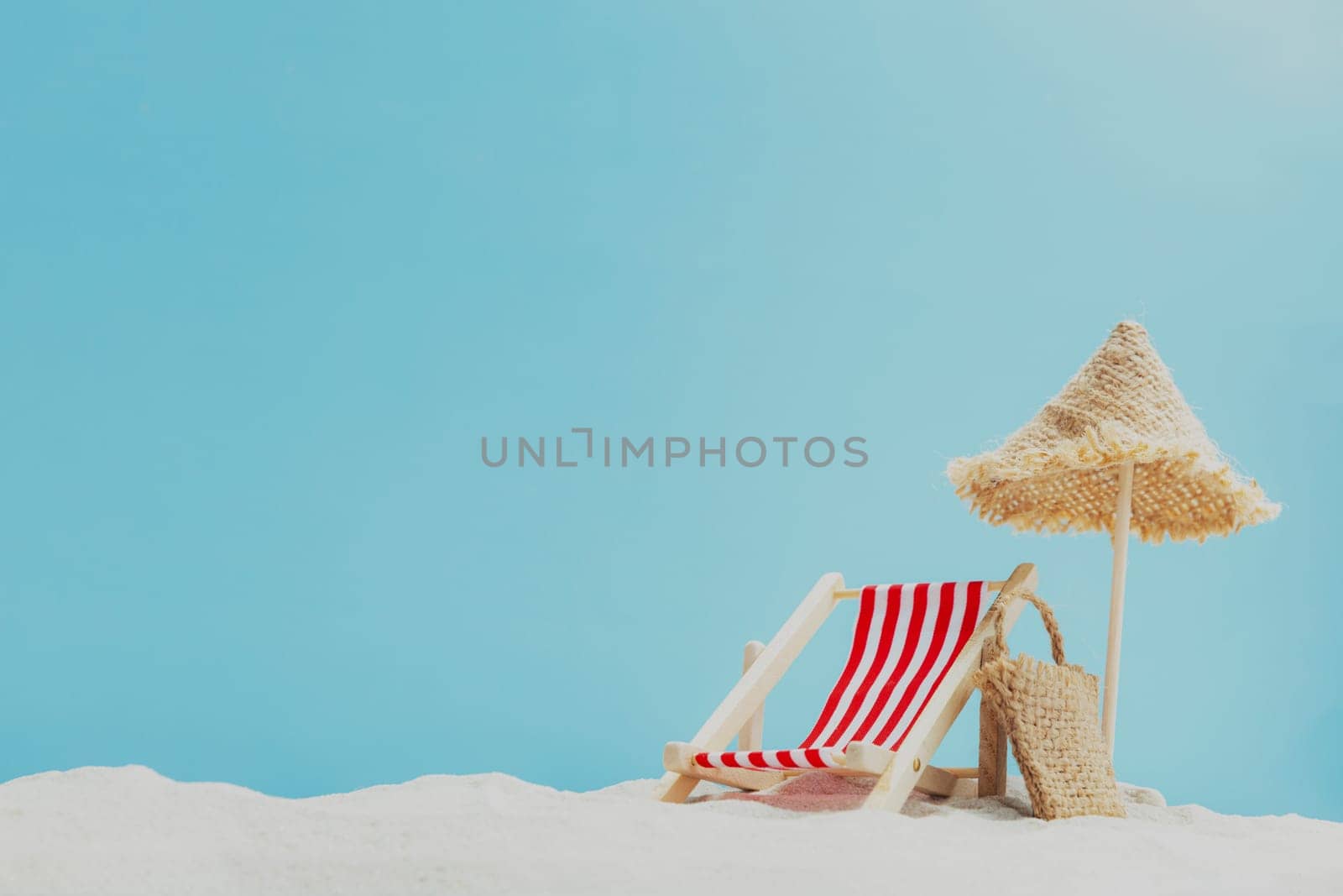 Vacation, beach, travel, relaxation concept. Symbolic background with beach sand, shell, mini sun lounger, beach chair, wooden lounge, beach bag, blue sky, sea or ocean. Minimalism with copy space