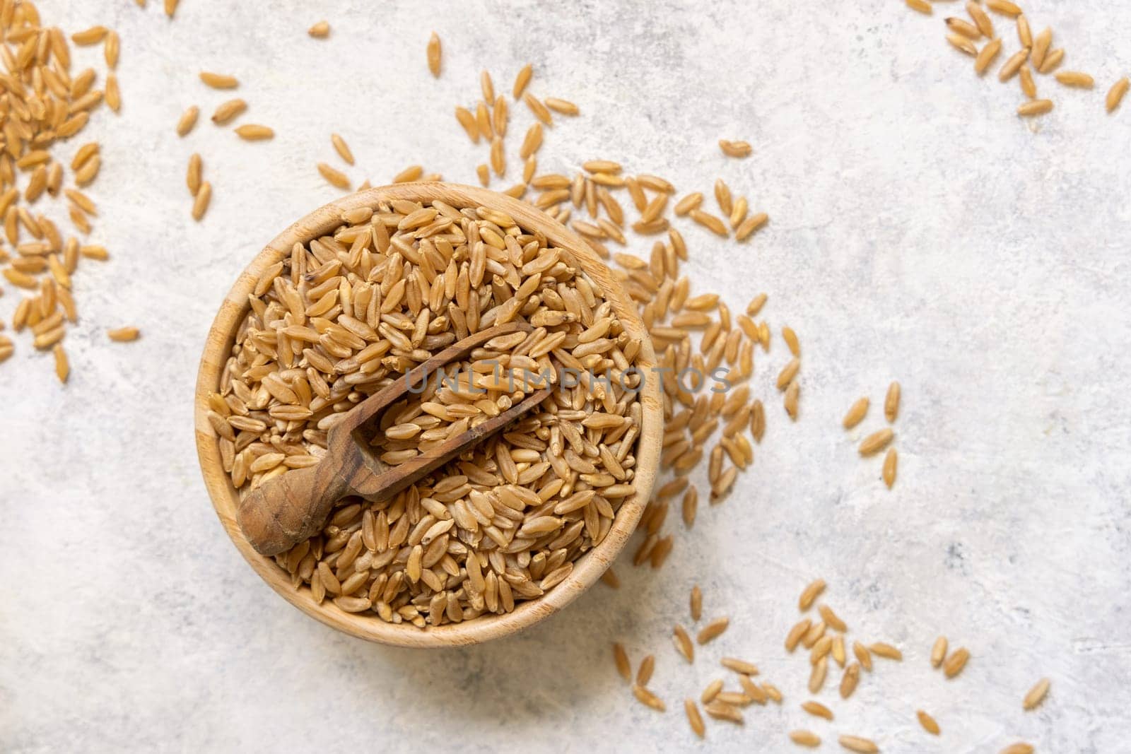 Bowl of raw dry rye grain with a wooden spoon on white table top view. Healthy alternative low gluten seeds. Protein source for vegan and vegetarian diet.