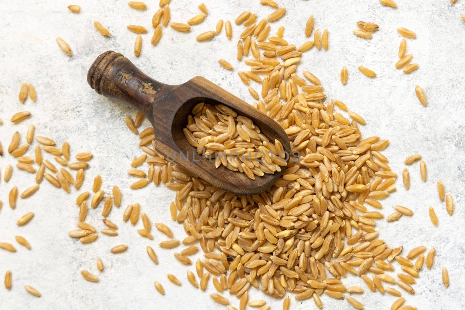 Wooden scoop of raw dry rye grain on white table top view. Healthy alternative low gluten seeds. Protein source for vegan and vegetarian diet.