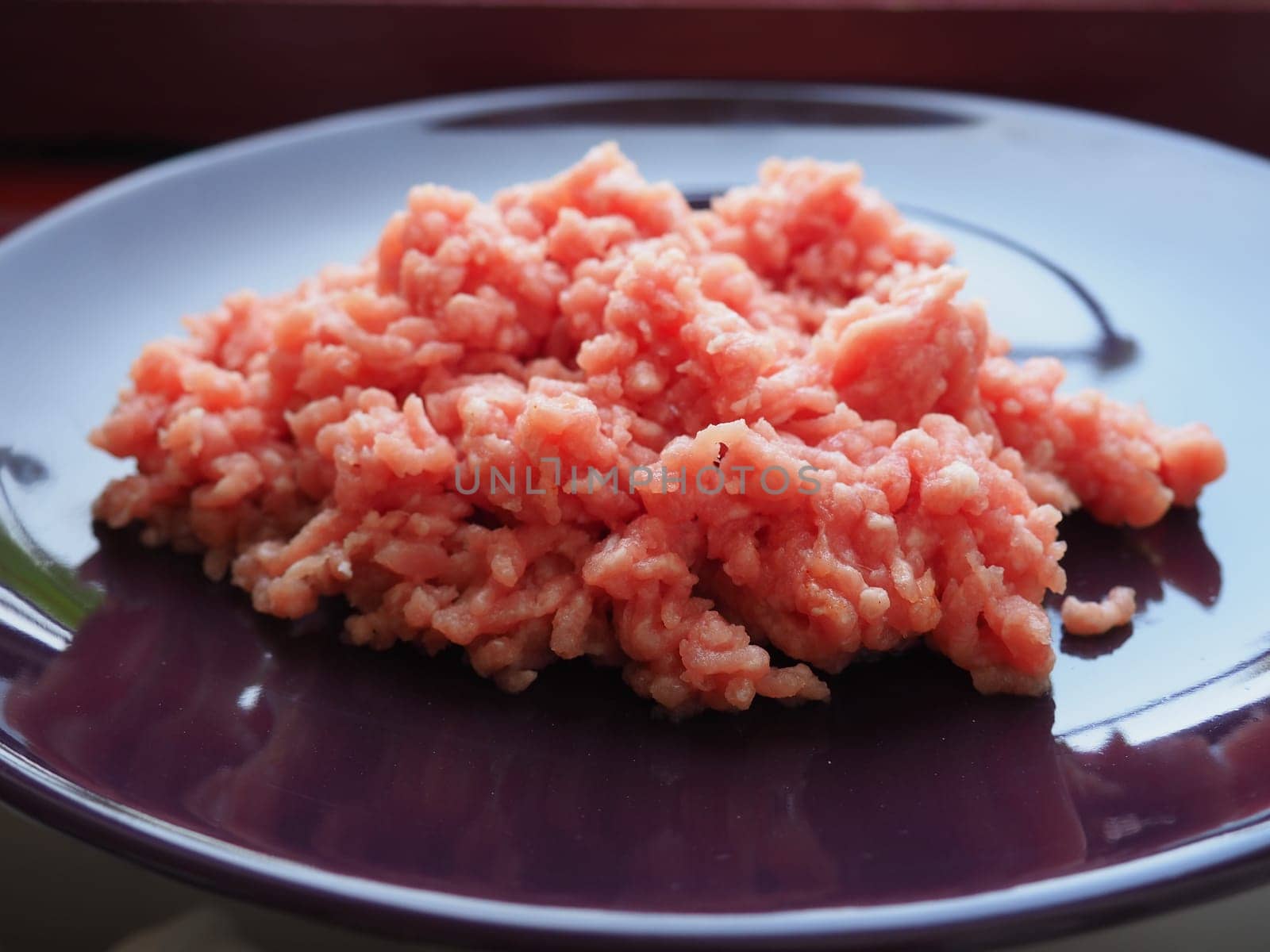 Minced meat on a purple ceramic large plate. Delicious fresh ground meat for making cutlets, steaks, hamburgers, meatballs. Pork semi-finished products.