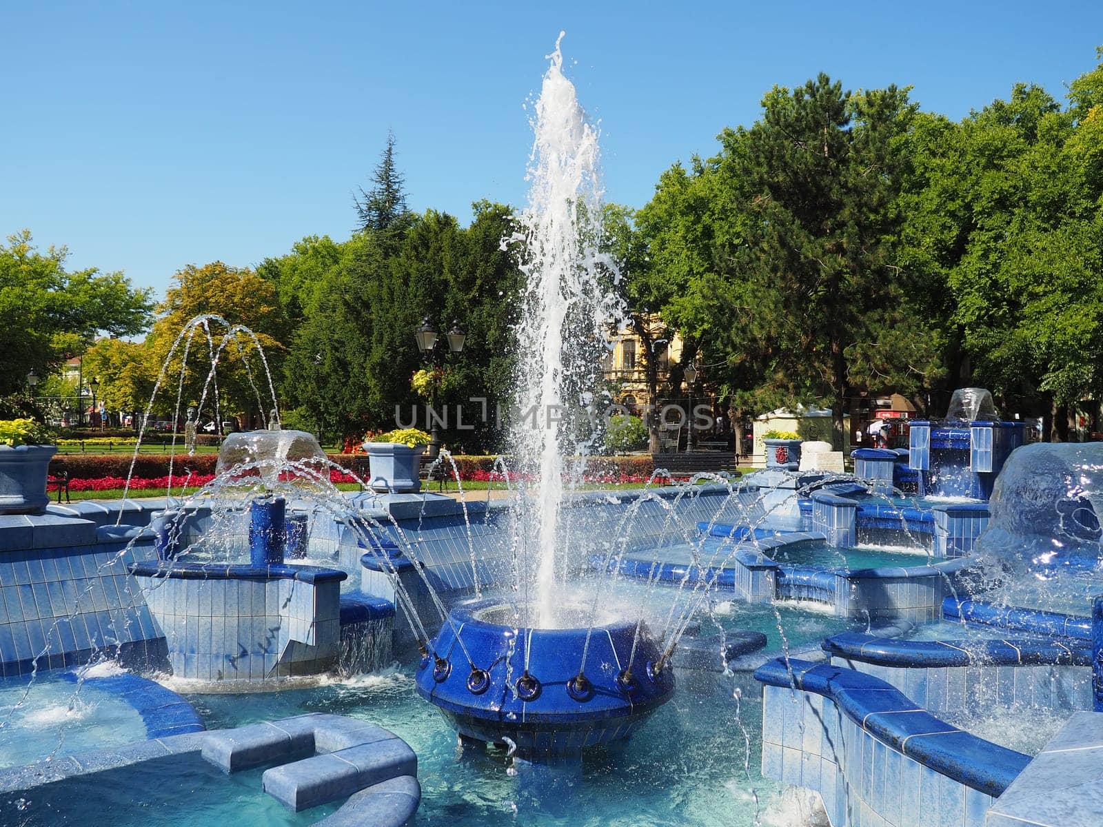 Subotica, Serbia September 12, 2021. Blue fountain in the square next to the Town Hall. Blue ceramic parts with monograms. A working fountain with splashing water. Summer sunny day by the blue water.
