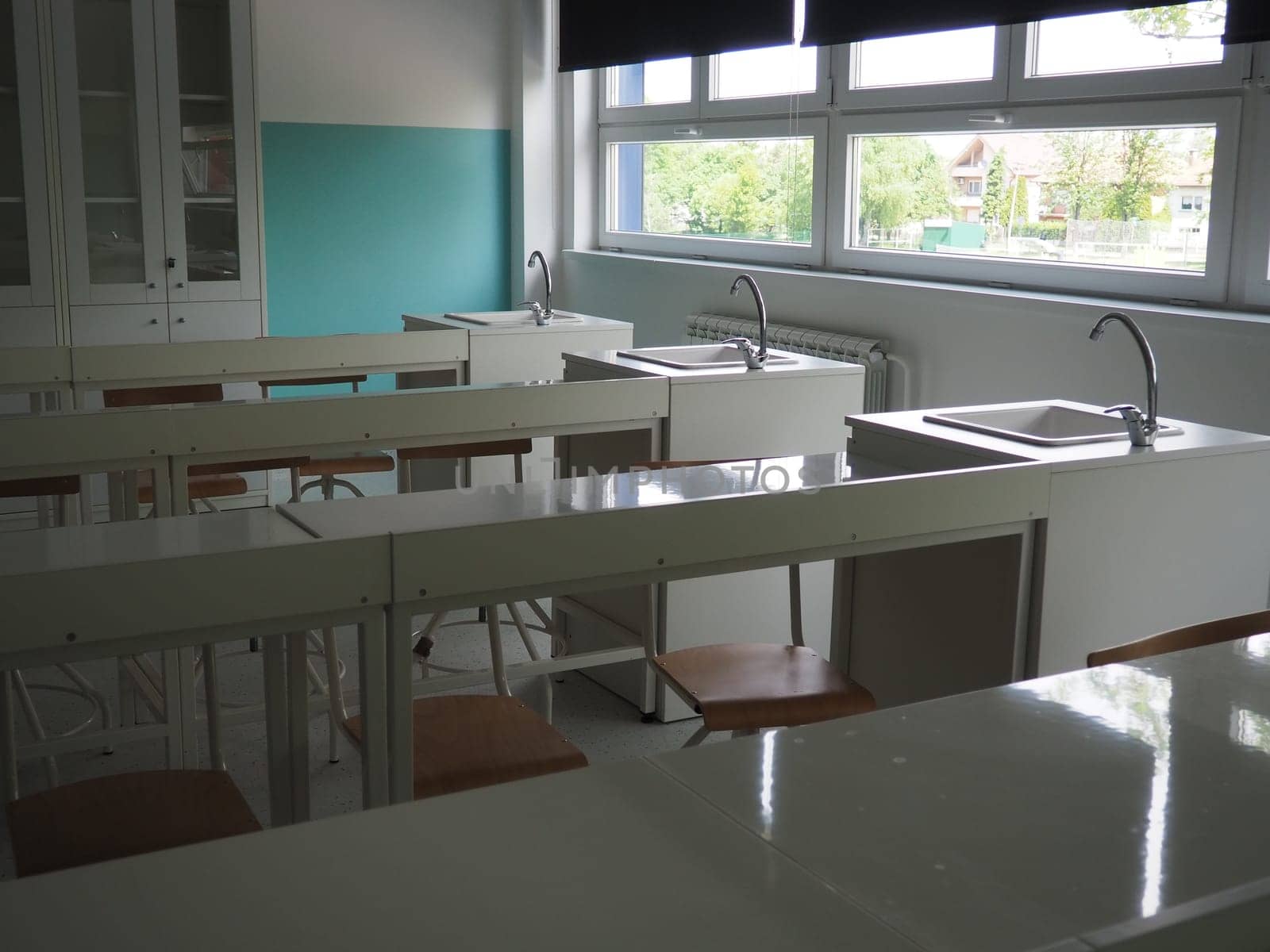 Chemistry room in a modern new school. Beautiful white furniture with sinks and washbasins. Large windows with blackout curtains or blinds. Empty school classroom. Furniture and school equipment.