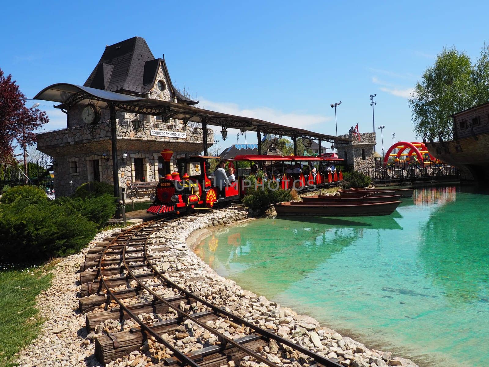 Stanisici, Bijelina, BiH, April 25, 2021. A children's steam locomotive with people and children drives passengers. The locomotive and the wagons are painted red. Summer amusement park.