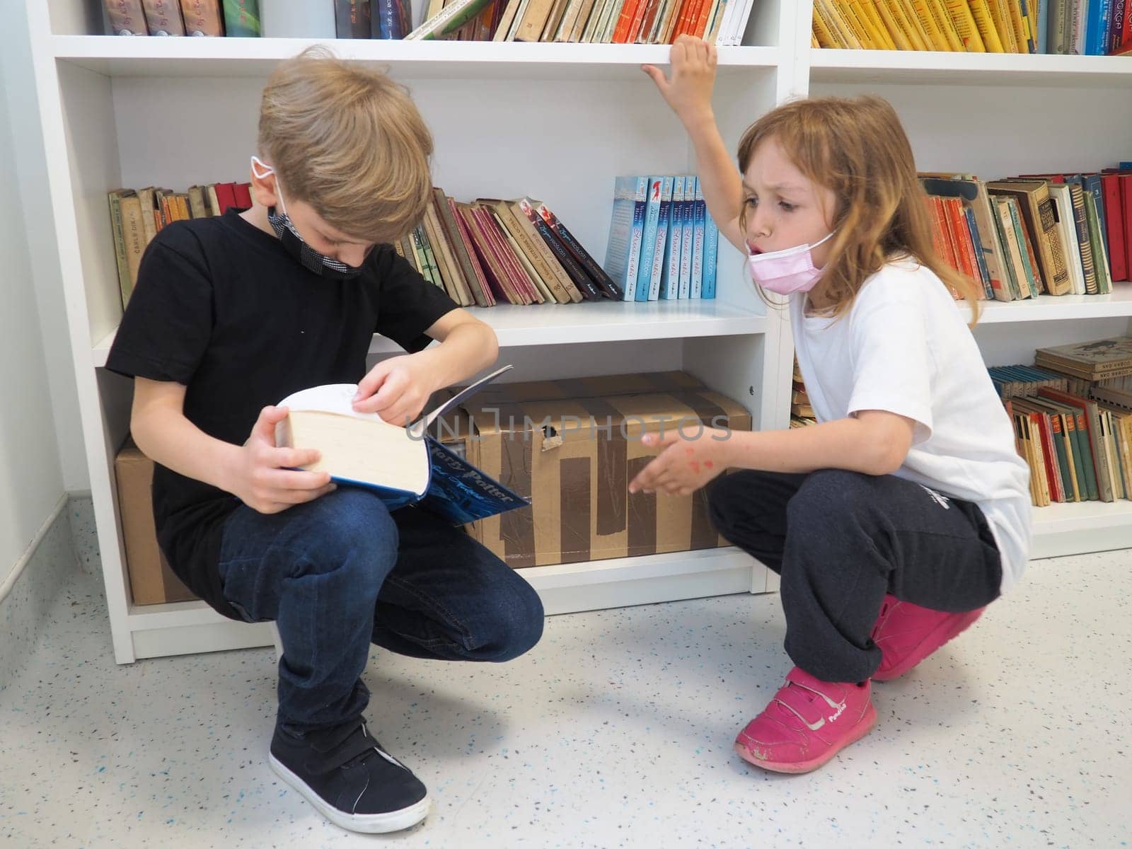 Sremska Mitrovica, Serbia, May 15 2021 Children in the school library. A boy and a girl search and leaf through books at the library rack. The boy is reading a very thick book. Schooling. Teens study.