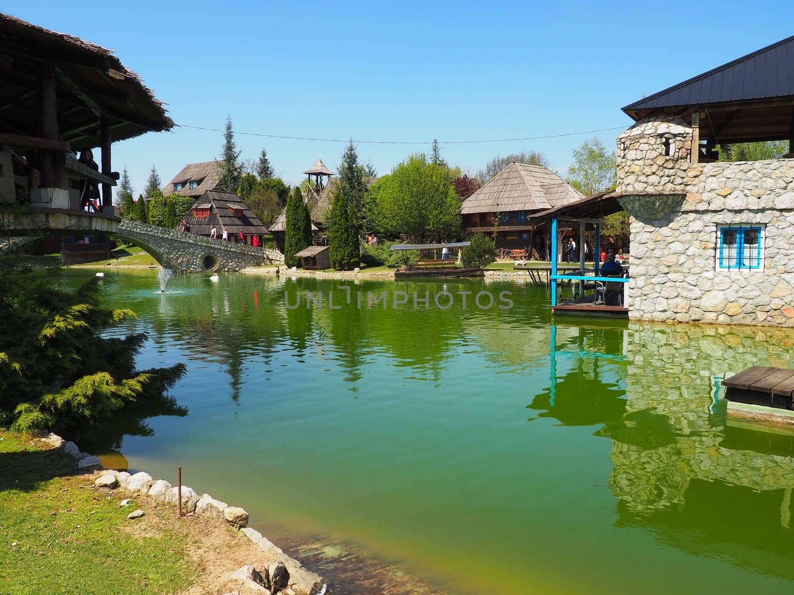 Stanisici, Bijelina, Republika Srpska, Bosnia and Herzegovina April 25, 2021 Ethno village, tourism and attractions. Stone and wood buildings and a bridge. Artificial pond with green water.