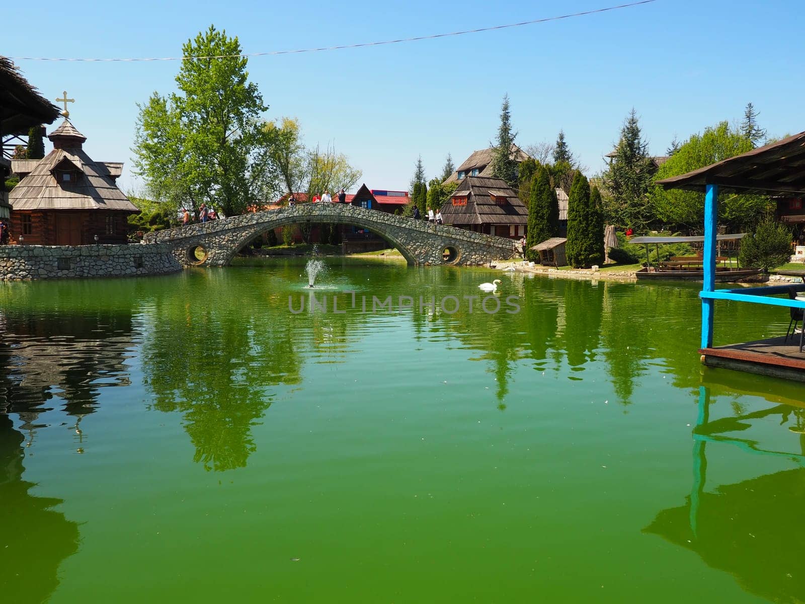 Stanisici, Bijelina, Republika Srpska, Bosnia and Herzegovina April 25, 2021 Ethno village, tourism and attractions. Stone and wood buildings and a bridge. Artificial pond with green water.