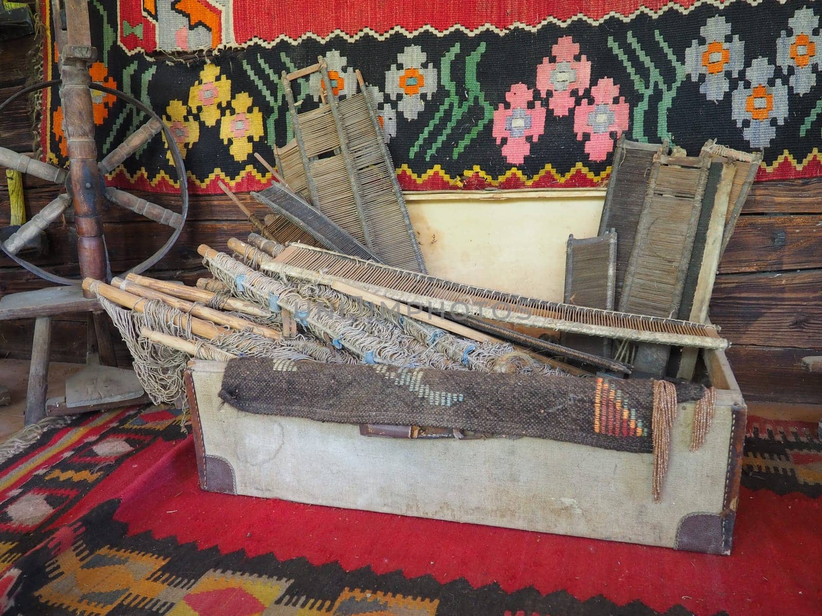 Antique carpet weaving tools. Carpet weaving in Serbia and Bosnia. Handicraft chest with wooden frames, foot spinning wheel. Log house wall with colorful carpets. Antique peasant theme. Work and hobby
