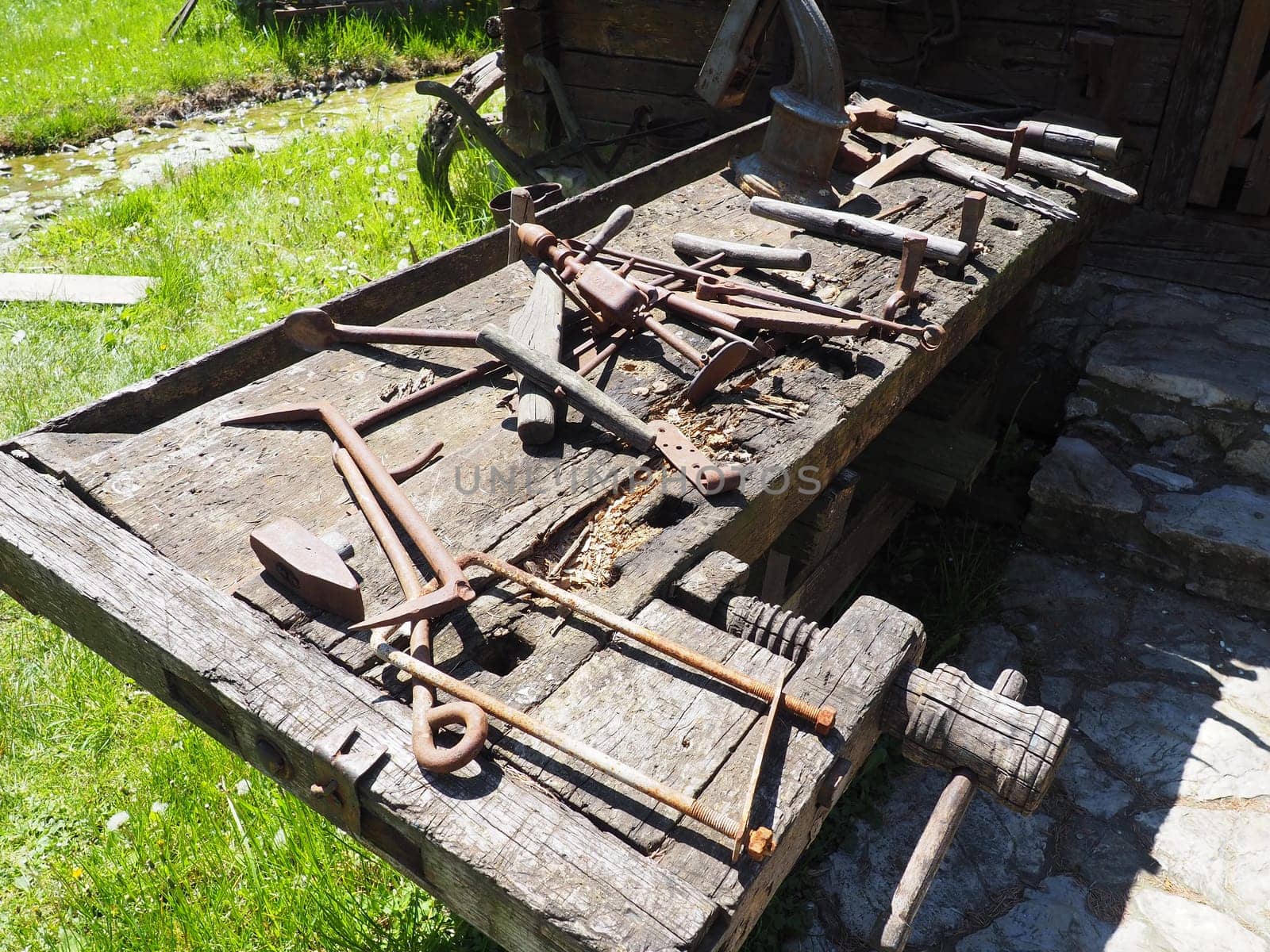 vintage working tools on a wooden table. Wooden and metal tools for building and rural life. Hammer, bracket, saw, ax, drill, tongs, poker, spoon, wooden vice. Village life. Joinery and carpentry.