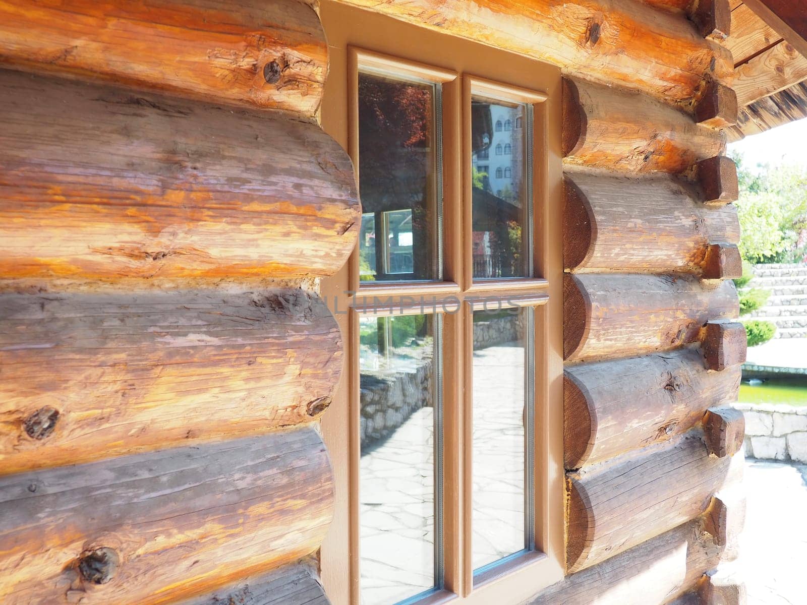 Fashionable log house close-up. Glass window with wooden frame. The wall of a wooden building with a canopy from the roof