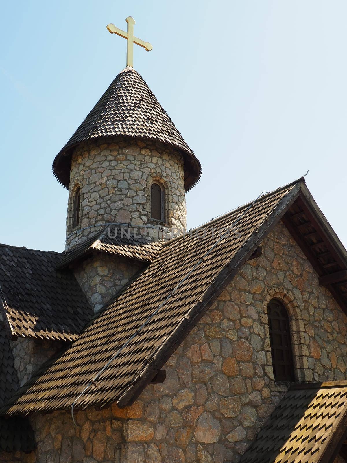 Stone Orthodox church in the ethno-park. Religious tourism. A building made of stones with a cross on the dome. Blue sky.