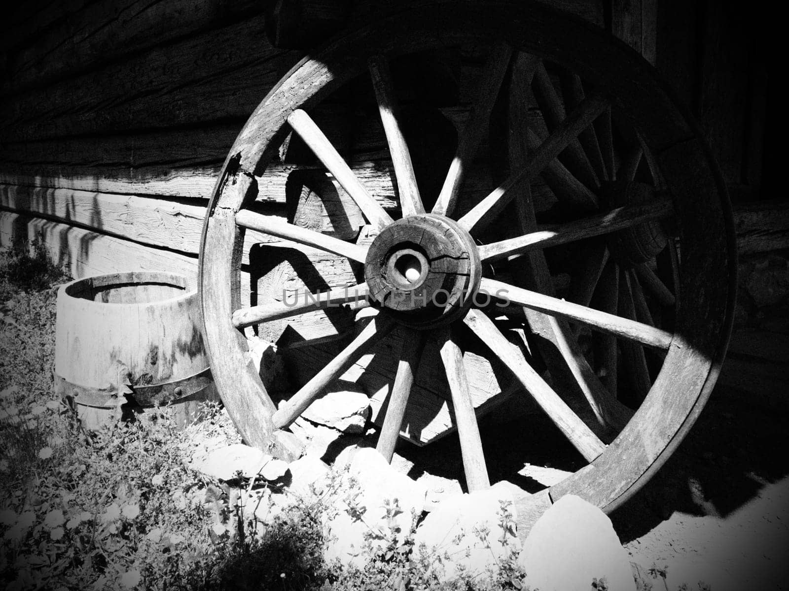 Wooden wheel from a cart. Decorative wheels for decorating lawns, exteriors and rustic interiors. Round homemade wheel against the wall. Retro or vintage style. Countryside life. Black and white.
