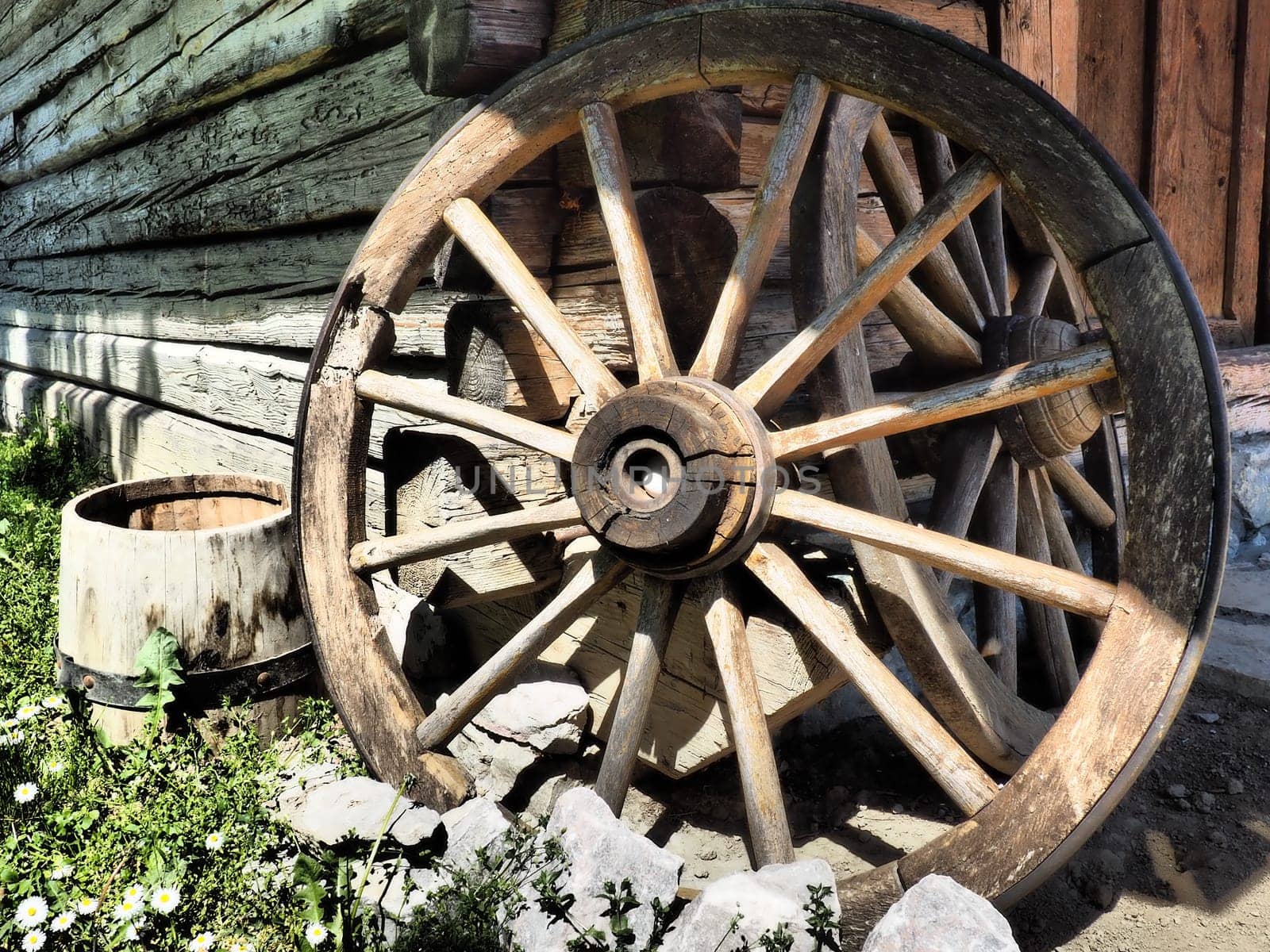 Wooden wheel from a cart. Decorative wheels for decorating lawns, exteriors and rustic interiors. Round homemade wheel against the wall. Retro or vintage style. Life in the countryside.