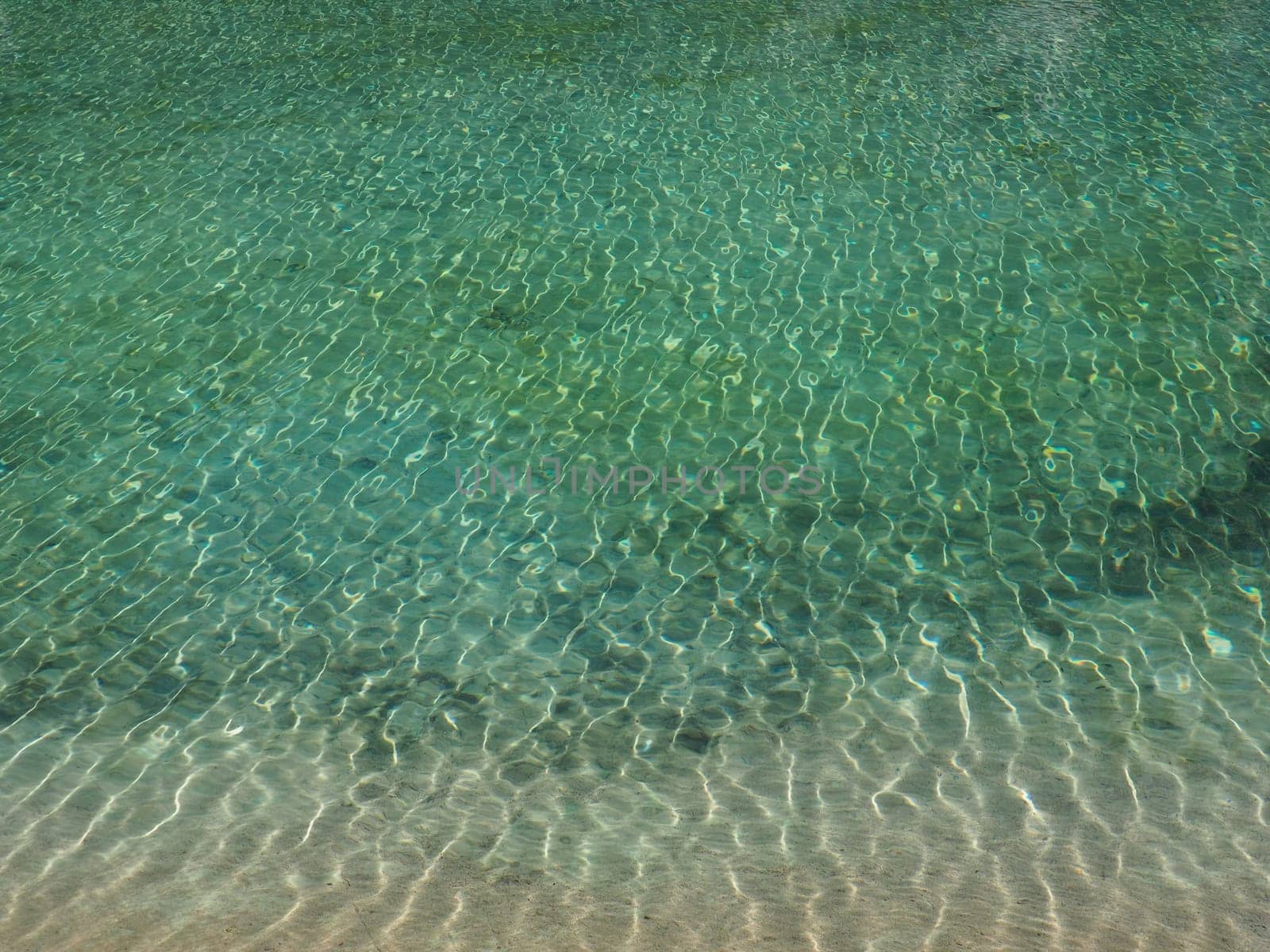 turquoise water. Clear sea water with waves and sun glare. The bottom is visible.