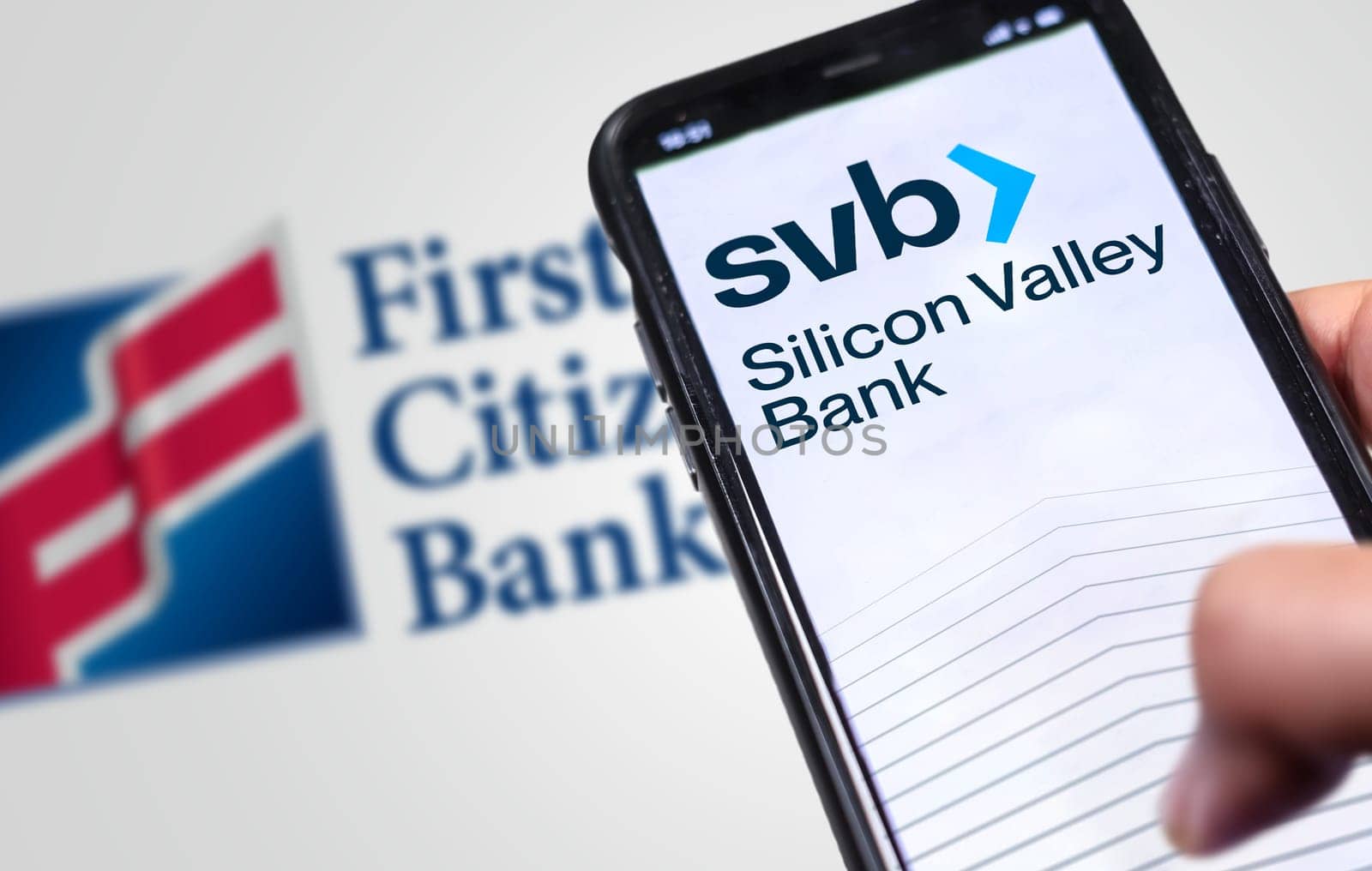 New York, US, March 2023: Hand holding a phone with Silicon Valley Bank logo on the screen with First Citizens Bank logo blurred on background. Illustrative editorial. Financial concept