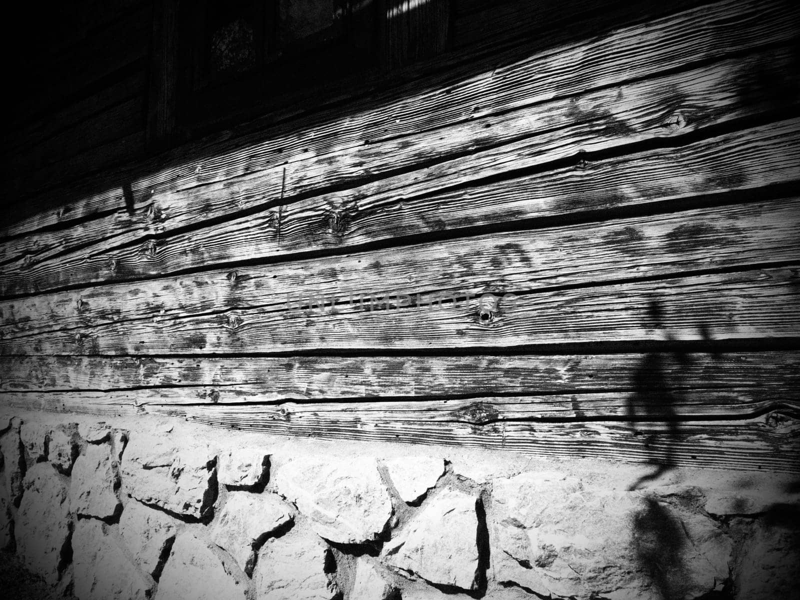 Log wooden wall of an old village house. Cobblestone foundation. Old methods of construction of residential buildings. Black and white photography, monochrome.