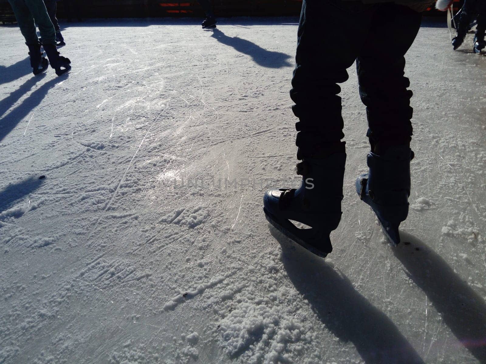 Feet with skates. Sports uniforms and equipment. Ice rink. Long shadows on ice from the low winter sun