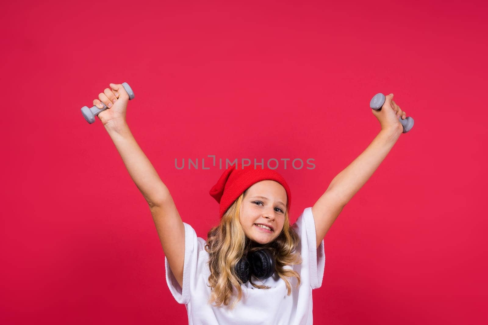 Kid girl doing fitness exercises with dumbbells on a red background