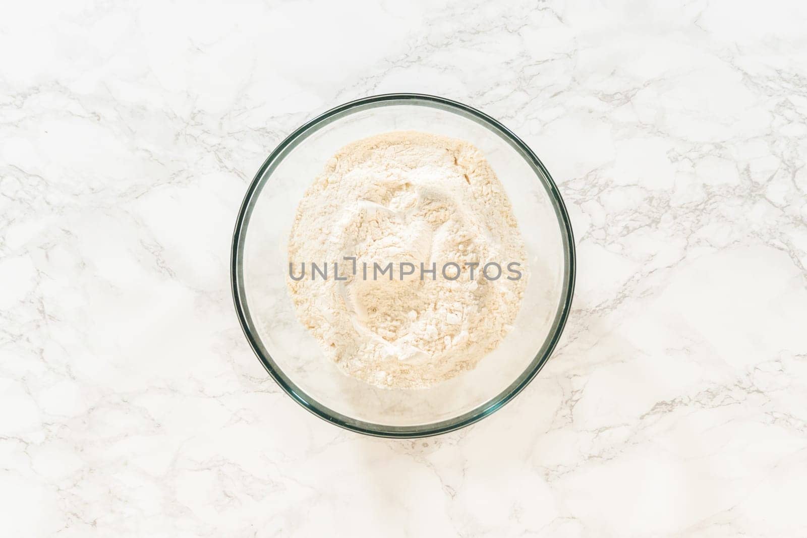 Top view of a mixing bowl filled with flour for Chocolate Ginger Sugar Cookie Dough preparation, sitting alone on a marble countertop.