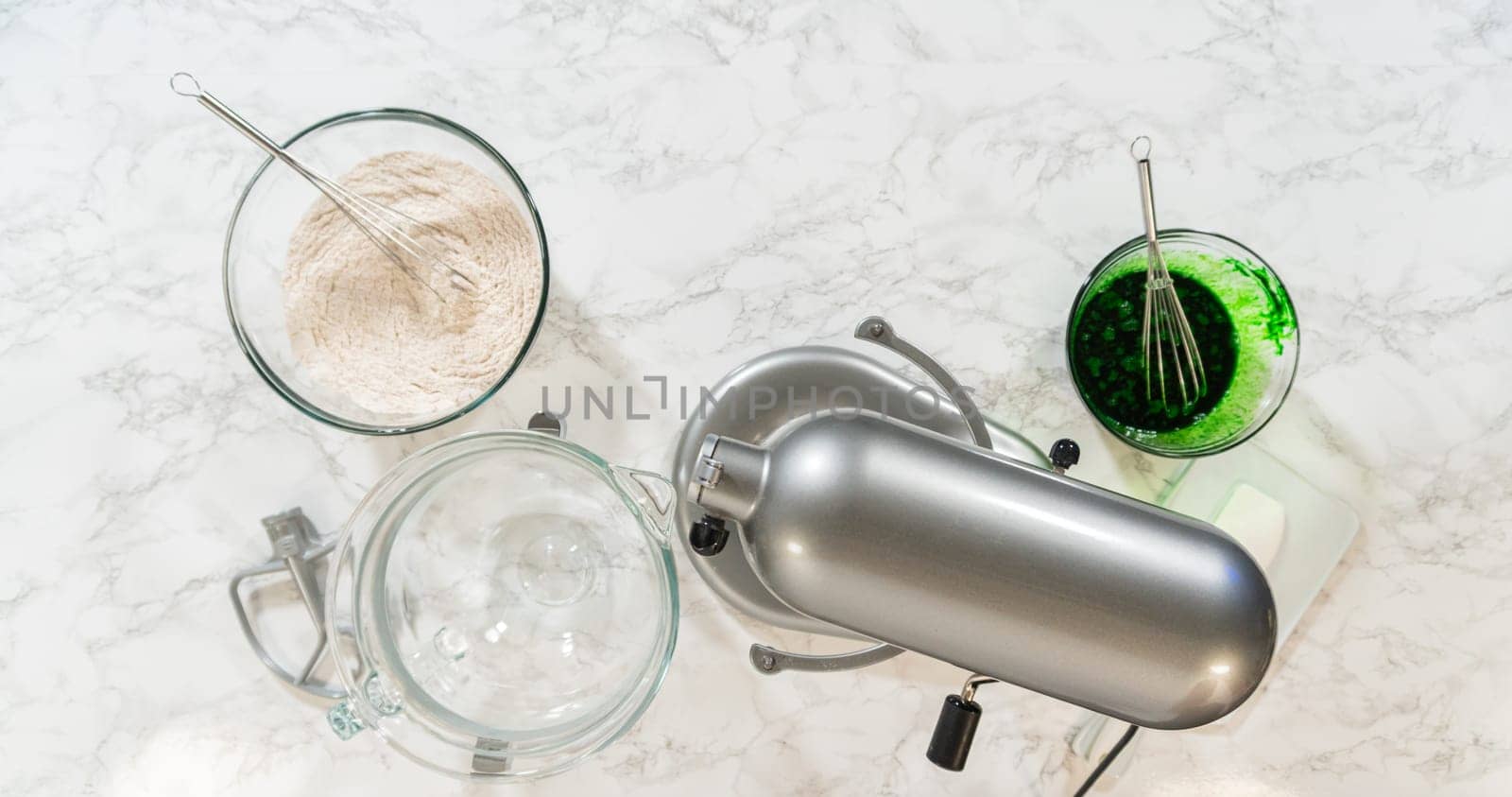 Ingredients organized around a stand mixer, ready to be combined for Vibrant Green Gingerbread Cookies for Festive Baking. Green color mixture and dry ingredients are set beside butter and sugar in the mixer bowl.