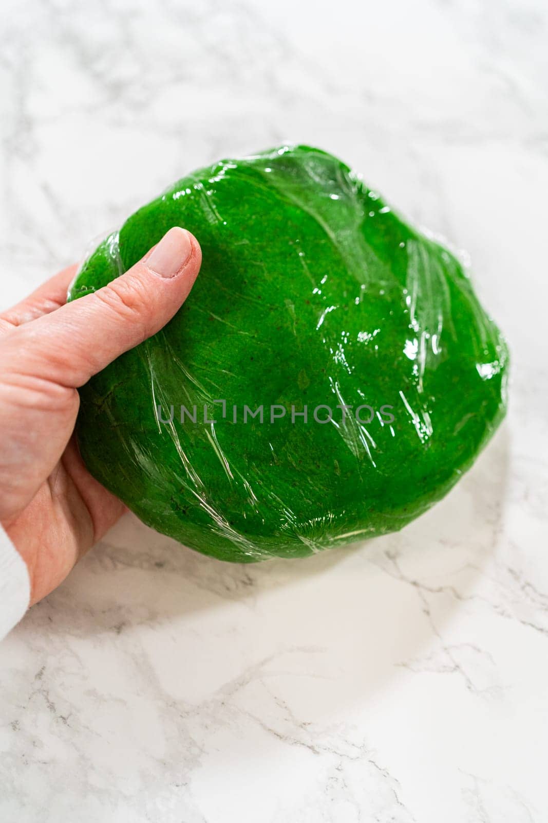 A single portion of green dough wrapped tightly in plastic wrap, ready for chilling before baking Vibrant Green Gingerbread Cookies for Festive Baking.