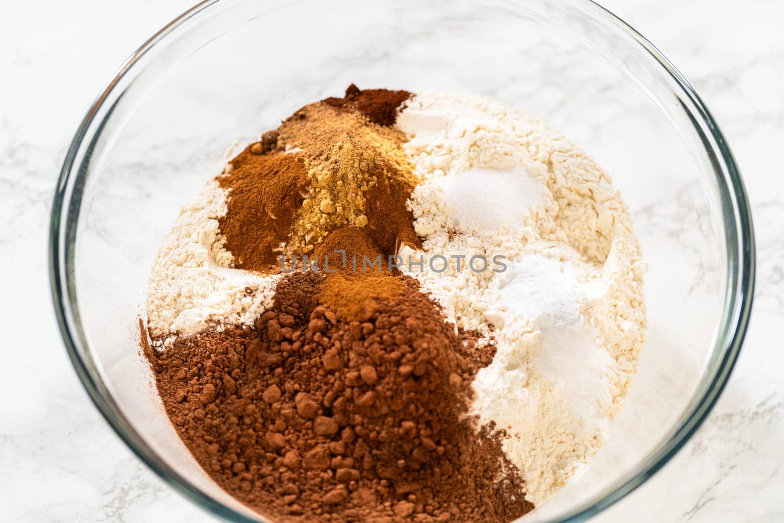 Mixing dry ingredients for Chocolate Gingerbread Cookie Dough, including flour, cocoa powder, cinnamon, ground ginger, and cloves in a glass bowl. The ingredients are layered and ready to be combined, creating a rich, aromatic base for the cookie dough.