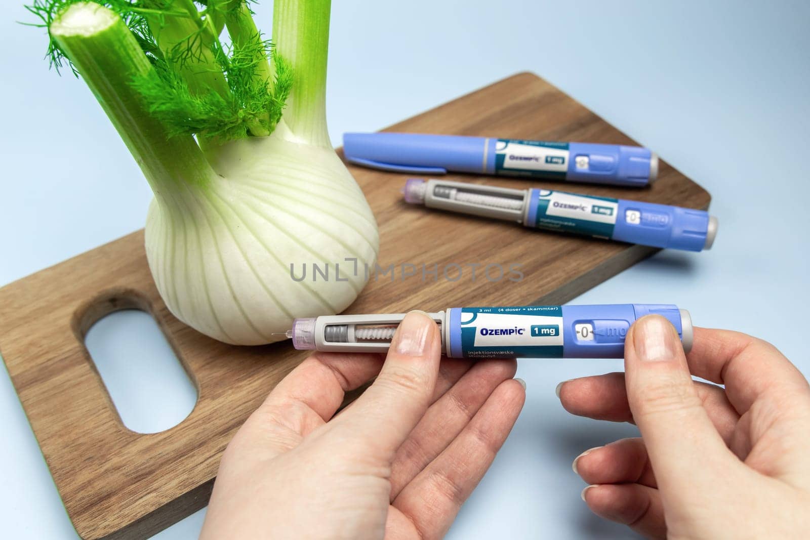 Hands holding Insulin injection pen and fennel vegetable root for diabetics and weight loss. Copenhagen, Denmark - February 16, 2025