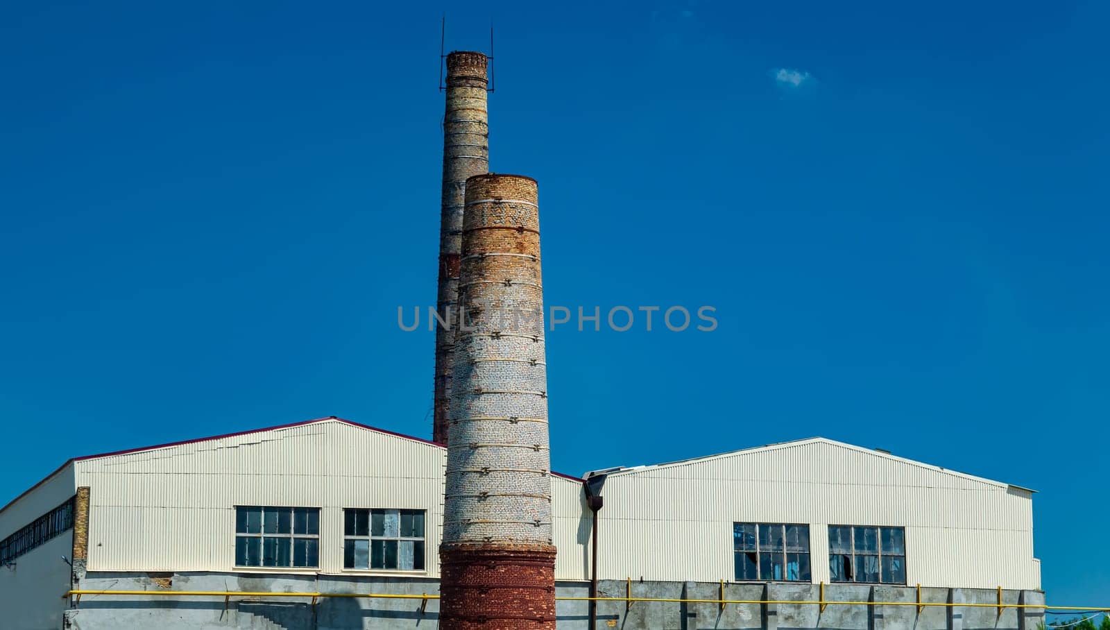 Industrial chimneys of the enterprise against the blue sky. Industrial chimney. Industrial factory building. Cloudless blue sky. Environmental protection. Ecological catastrophy.