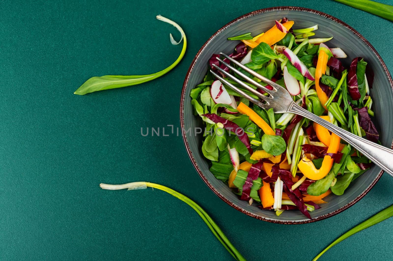 Healthy salad bowl with vegetables and bear leek or wild garlic on a rustic wooden board.