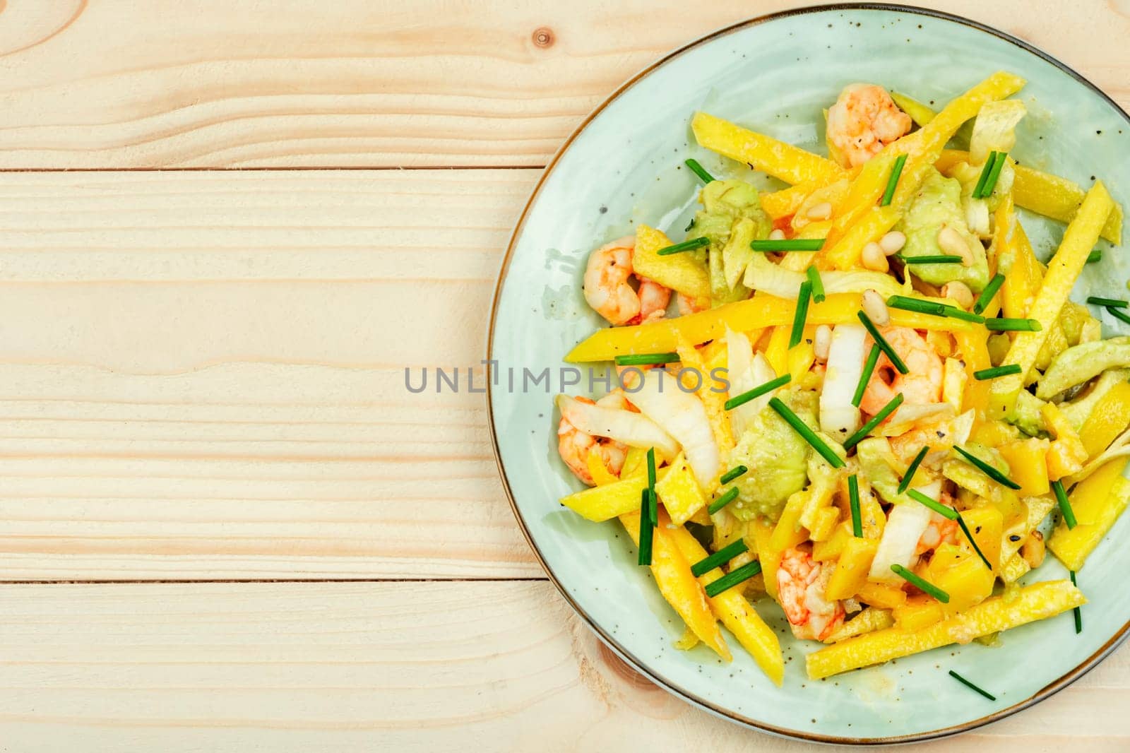 Delicious salad of mango, avocado, shrimp and pine nuts served on plate.
