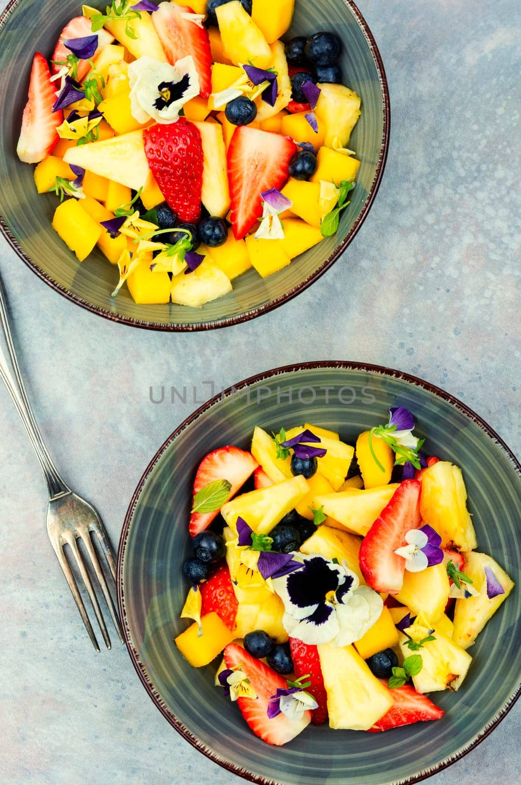 Vegan salad of pineapple, strawberries and berries, decorated with edible flowers. Top view.