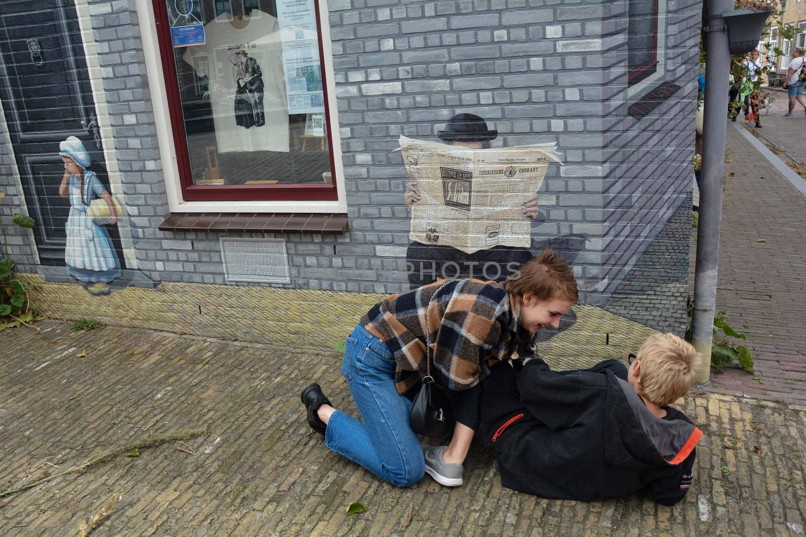 Zierikzee, Zeeland, The Netherlands , August 27th 2020 - House facade with artistic mural of a man reading the newspaper at the Plein Montmaertre in the middle of the city . Two children are lying on the floor fooling around