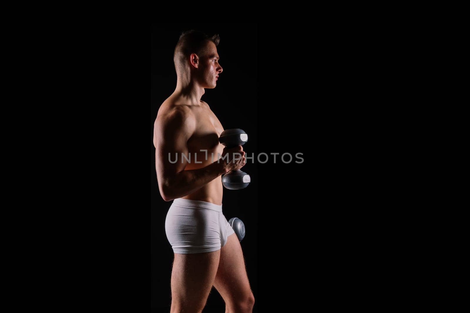 Shirtless bodybuilder holding a dumbell and showing his muscular arms.