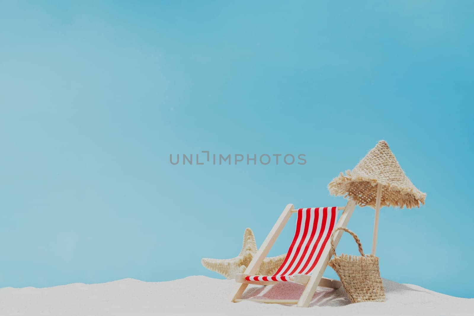 Vacation, beach, travel, relaxation concept. Symbolic background with beach sand, shell, mini sun lounger, beach chair, wooden lounge, beach bag, blue sky, sea or ocean. Minimalism with copy space