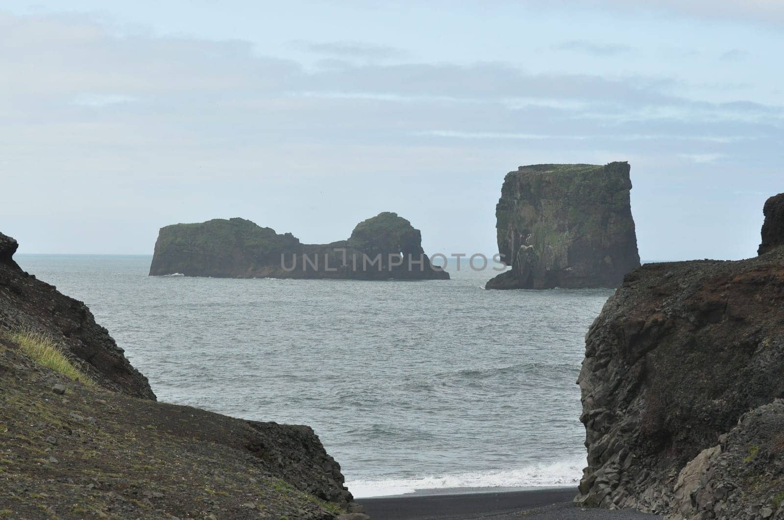 Scenic view of Icelandic coastline with waves hitting huge black rocks at overcast Dyrholaey Cape