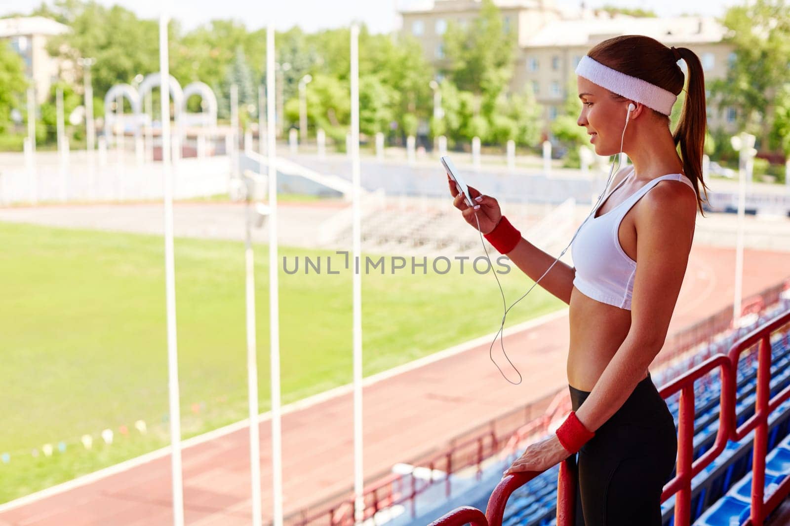 Sporty girl with earphones and iphone visiting stadium