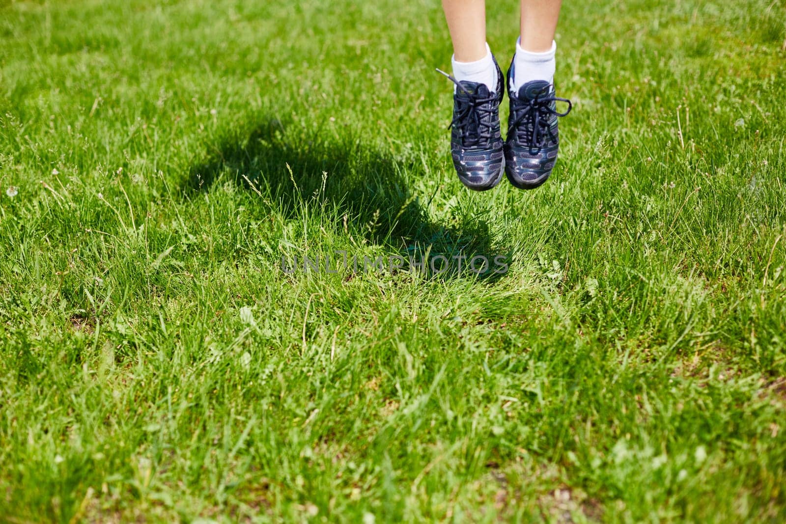 Feet of woman in sports-shoes jumping over green lawn