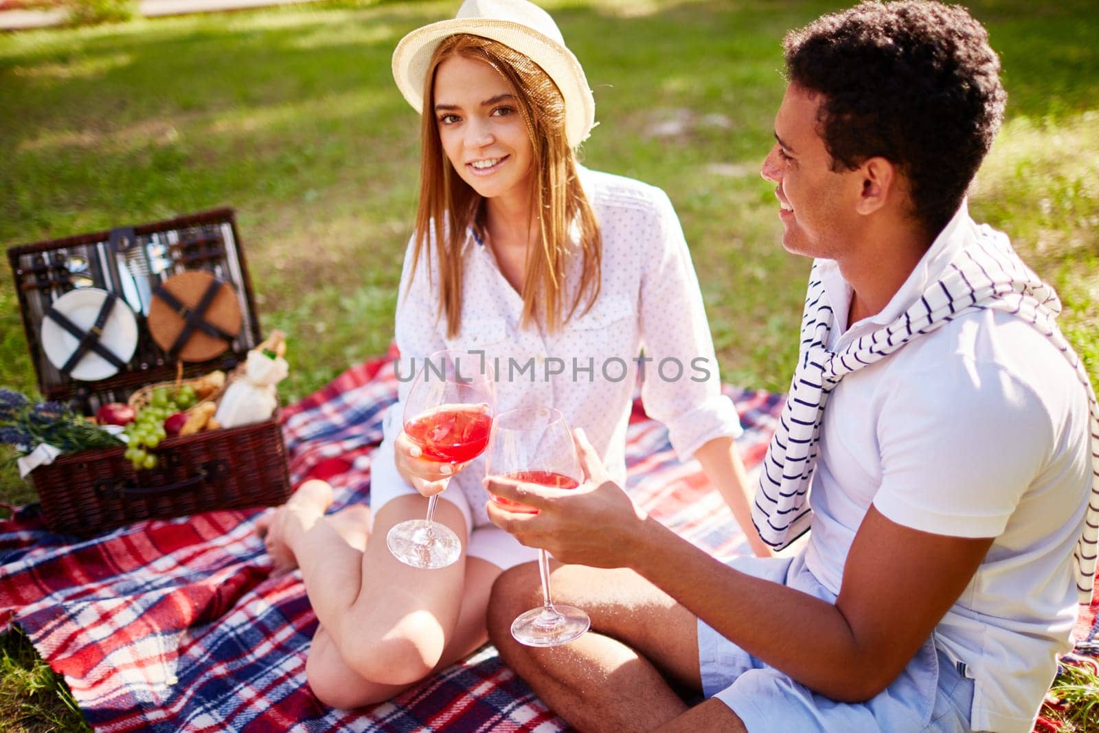 Happy girl with red wine looking at camera during romantic date with her boyfriend in park