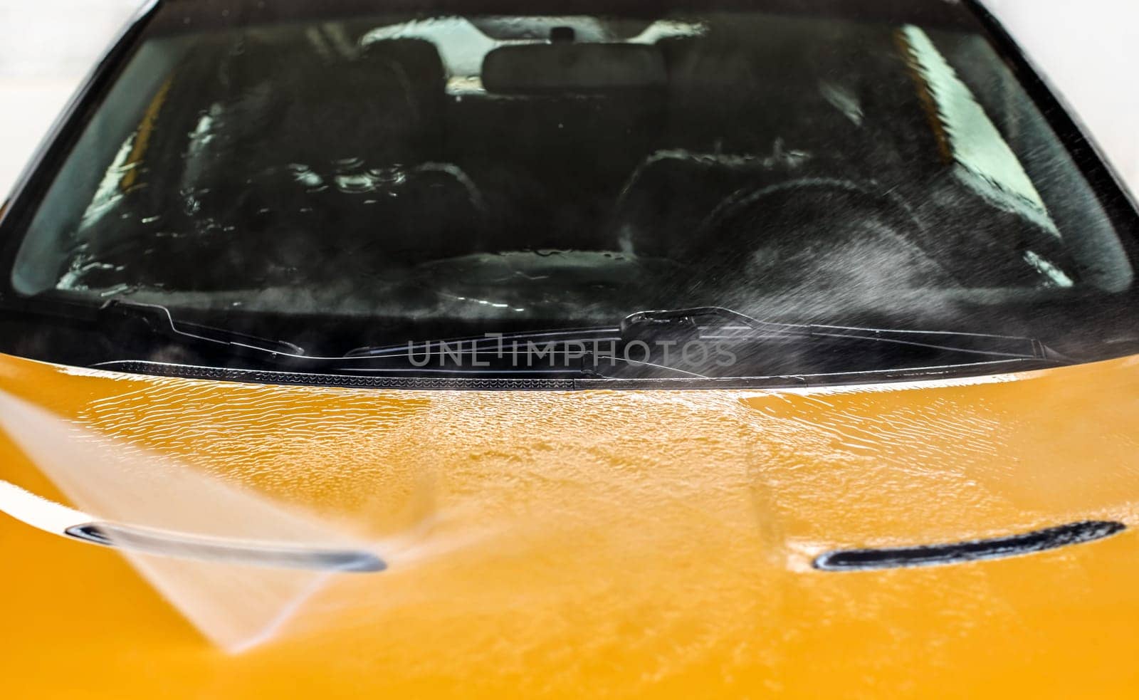 Water jet spraying on front of yellow car washed in self serve carwash.