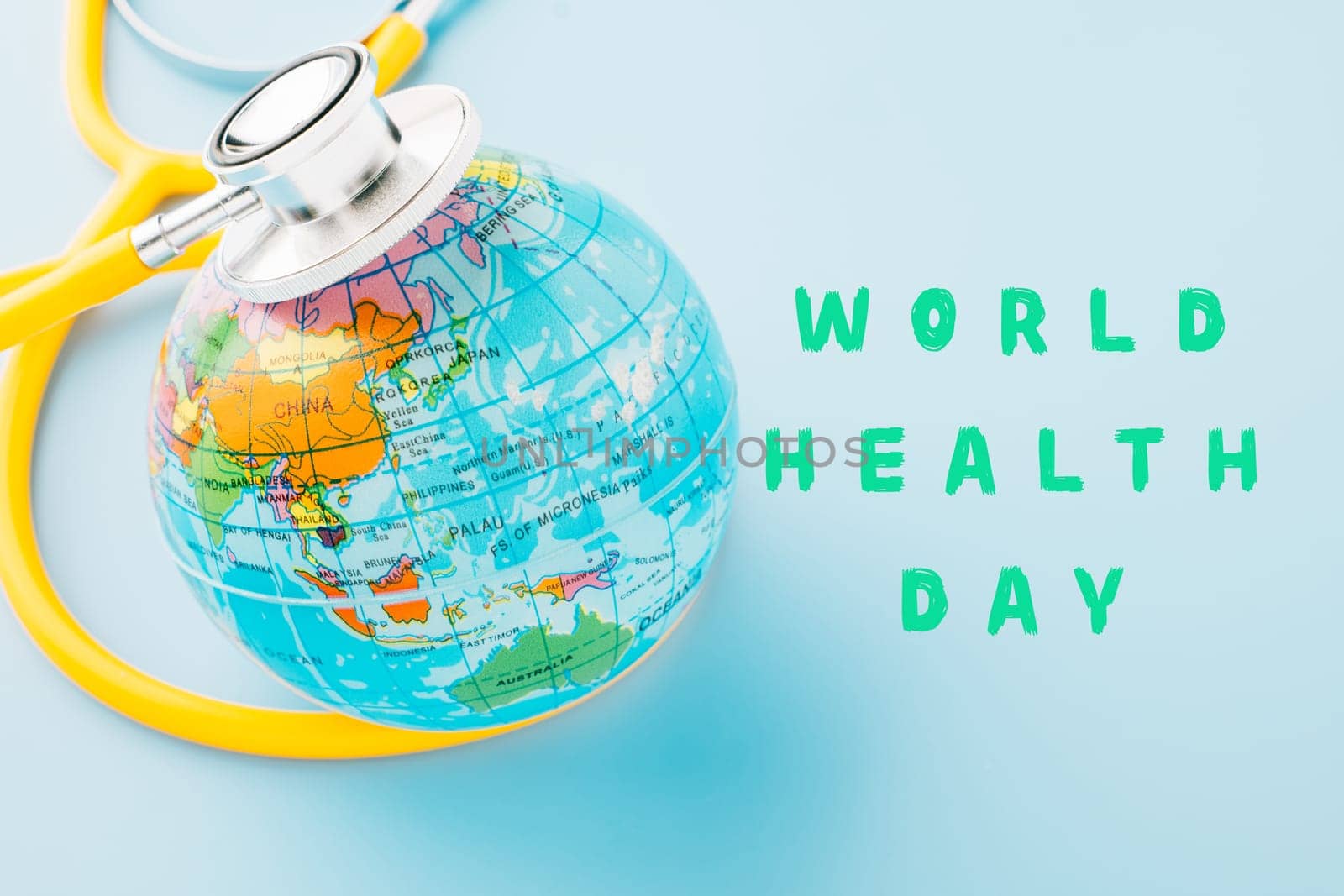 World Health Day Concept. Top view yellow doctor stethoscope and world globe isolated on pastel blue background with copy space, Save world day, Environment Green Earth, Health care and medical