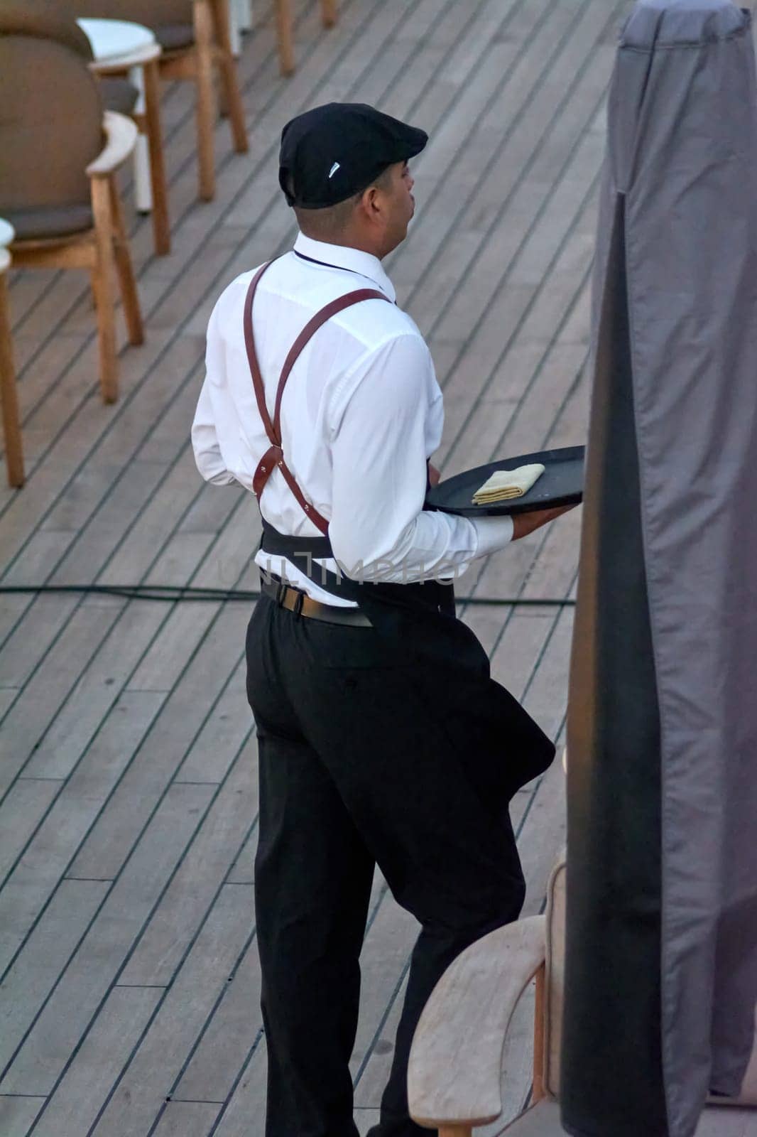 Civitavecchia, Italy - February 18, 2025: Waiter balances a tray on an elegant wooden floor, highlighting the sophistication and poise of a well-trained service professional in a refined setting.