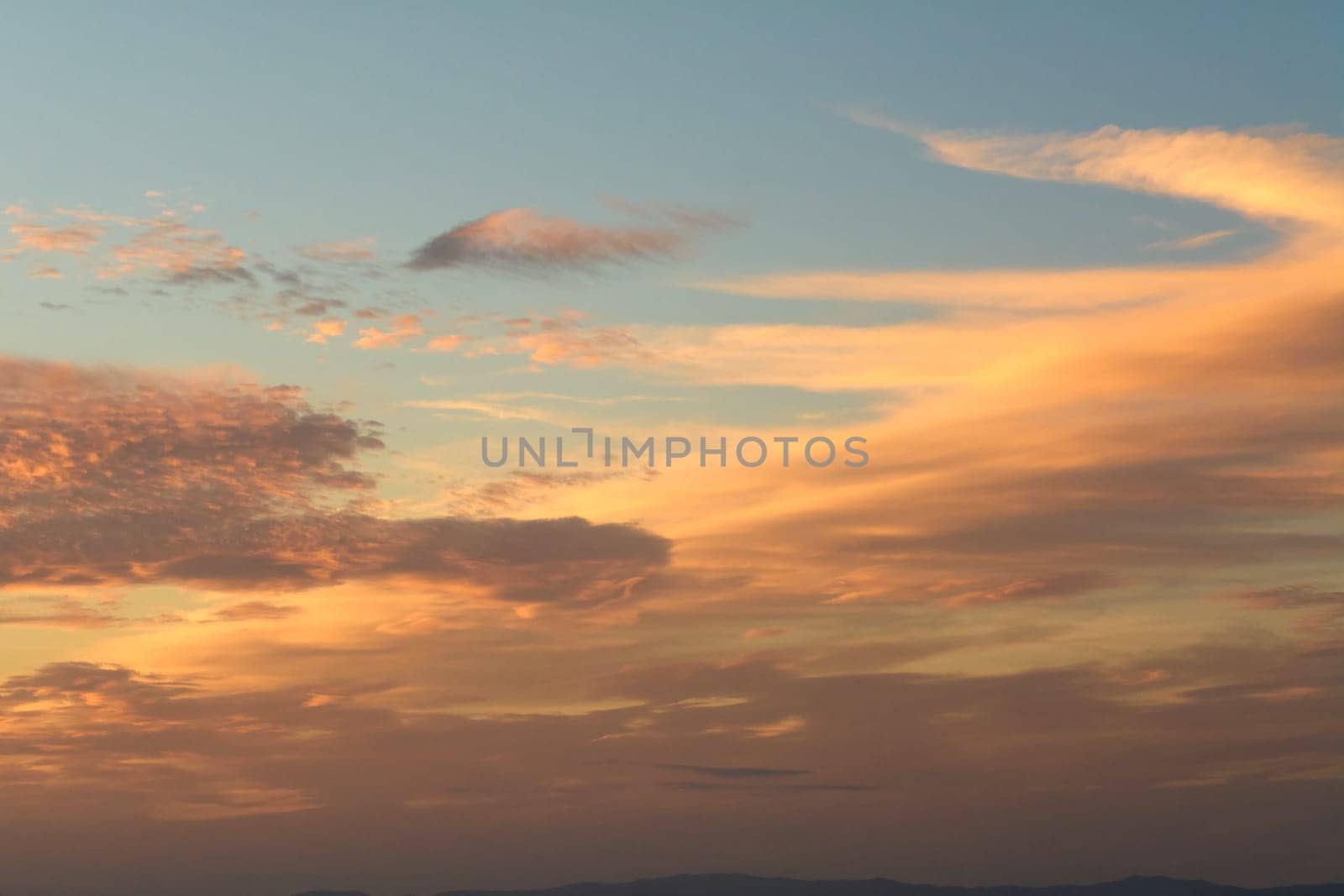 A picturesque sunset scene with clouds scattered across the sky, reflecting warm hues of orange and yellow over a body of water. Perfect for themes of nature's beauty and tranquility.
