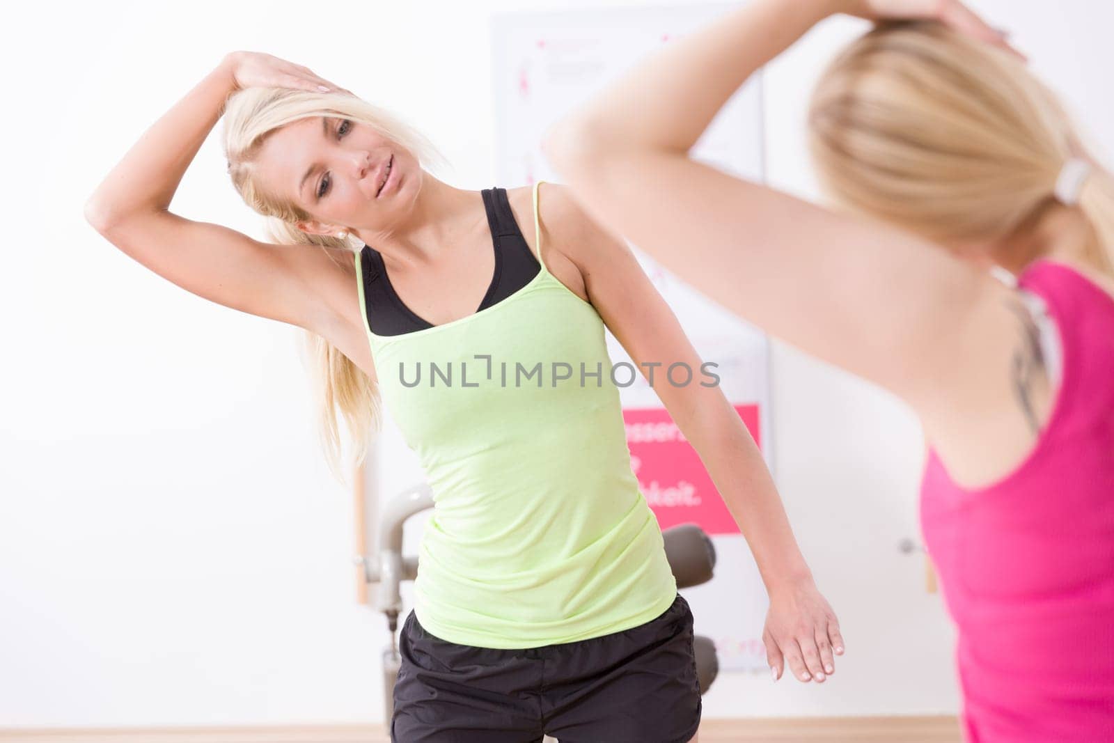 Two young women do stretching out in a gym