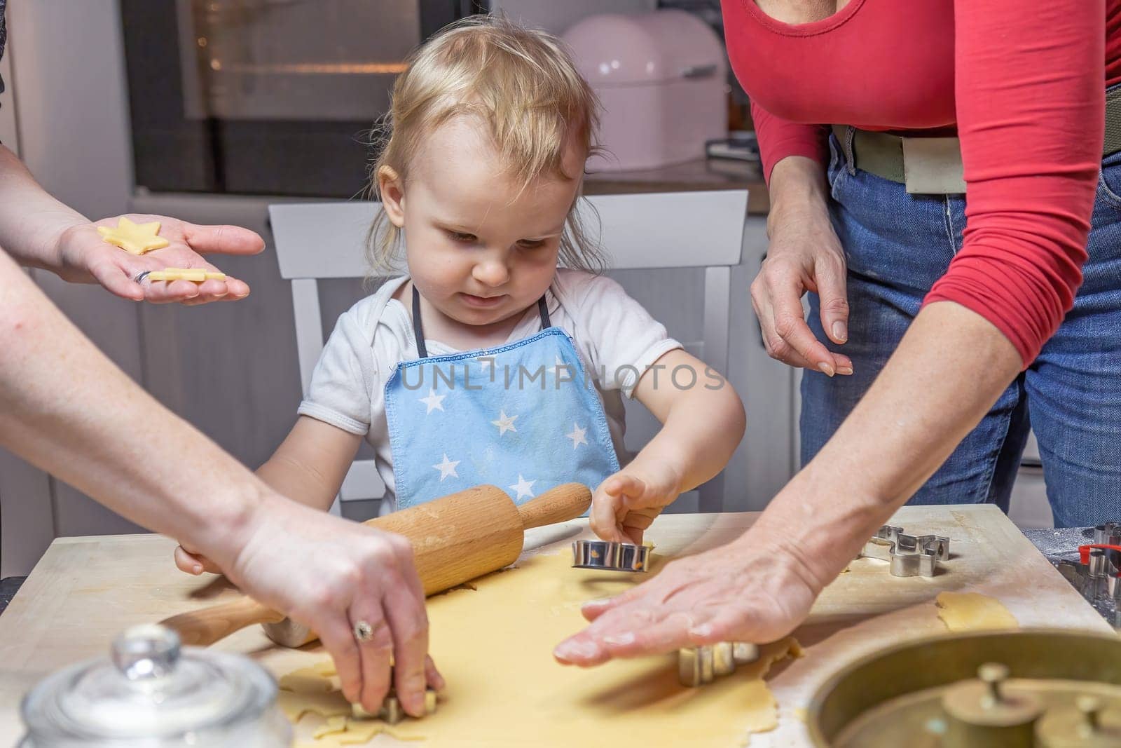Little child boy is helping two women in baking in domestic kitchen.
