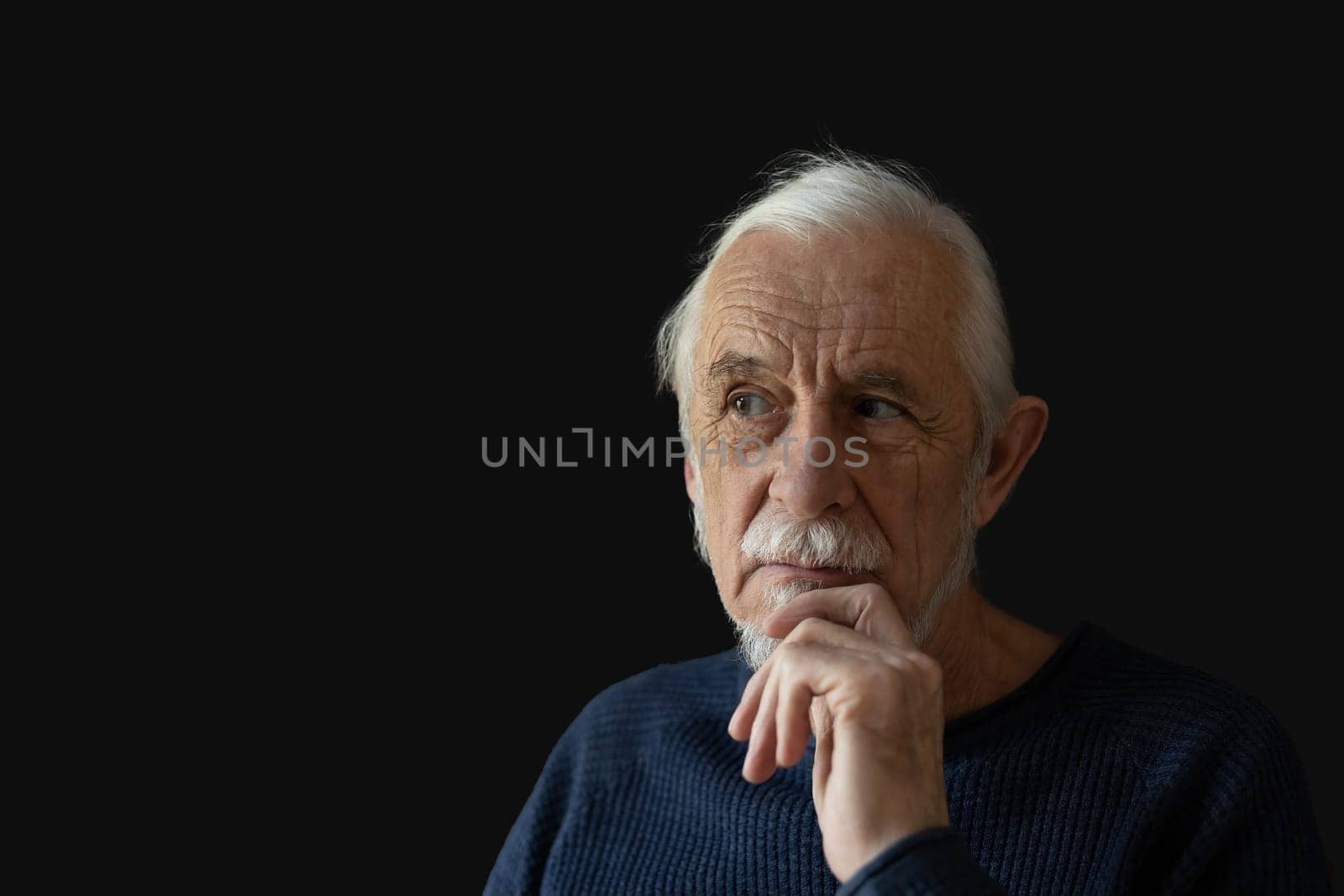 Beautiful gray hair old man wirh wrinkled face is posing on black background peeking to the right. Horizontally.