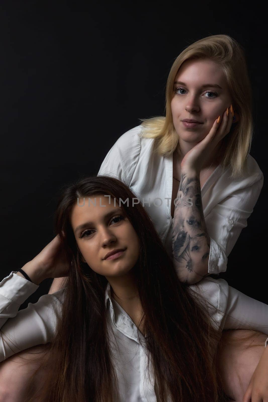 Low key portrait of two beautiful young women sitting in the studio. Vertically.