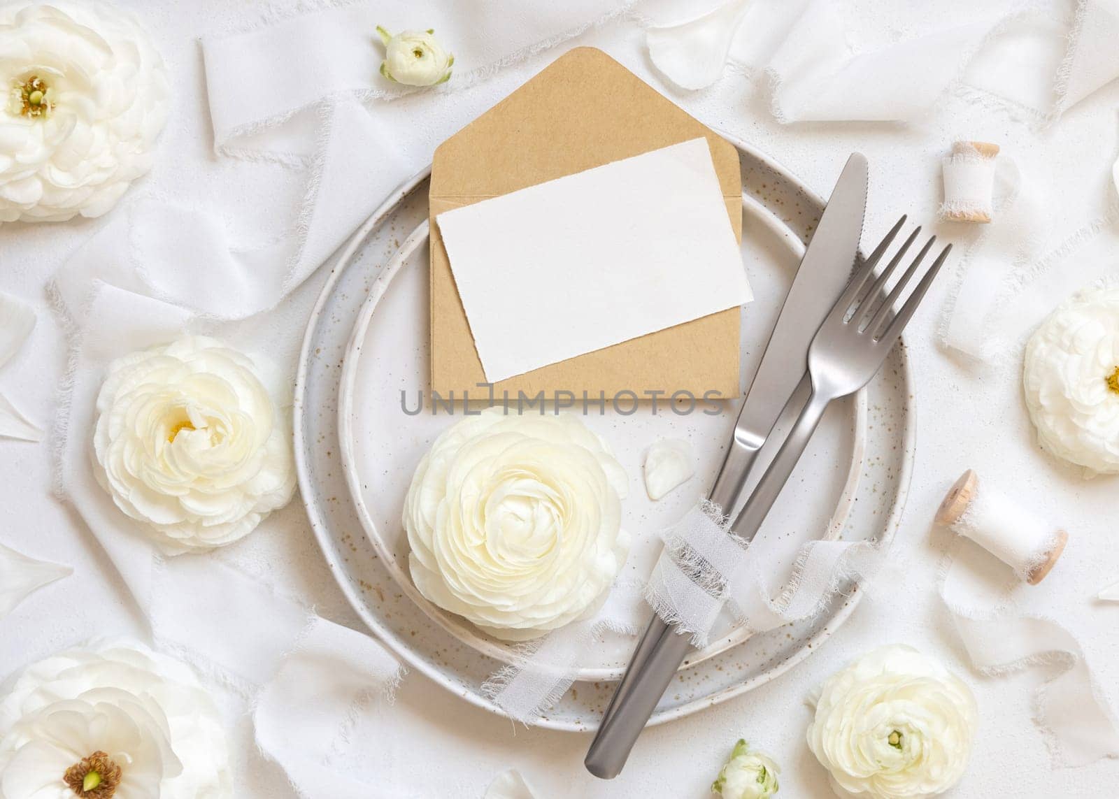 Wedding table setting with card and envelope near cream roses and white silk ribbons top view, mockup. Romantic scene with horizontal table place card and pastel flowers. Valentines, Spring or Mothers day concept