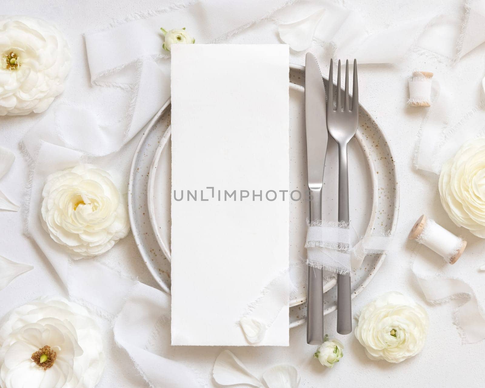 Wedding table setting with card near cream roses and white silk ribbons top view, mockup. Romantic scene with vertical menu card and pastel flowers. Valentines, Spring or Mothers day concept