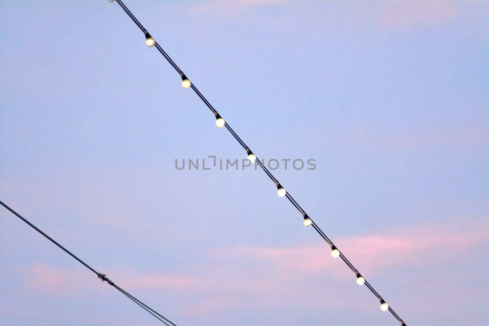 A row of glowing string lights suspended on a cable, set against a gradient sky transitioning from light blue to pinkish hues. The scene captures the serene and magical atmosphere of twilight.