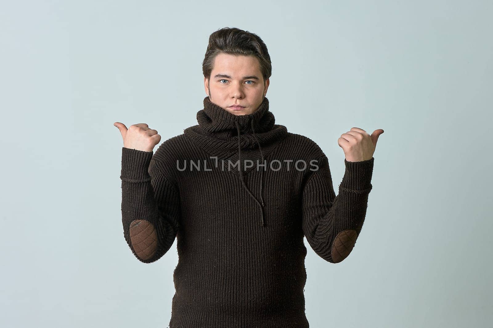 A man in a brown sweater on a gray background raised his hands. High quality photo